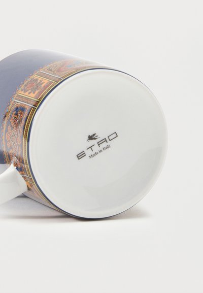 Tasse en céramique blanche avec un motif orné coloré sur le côté, allongée sur le côté avec le logo "ETRO Made in Italy" visible en bas.