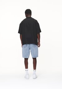 Una maglietta nera a maniche corte con una vestibilità comoda, abbinata a pantaloni corti in denim azzurro. Il modello indossa sneakers bianche e calzini alla caviglia.