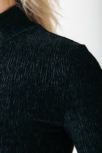 Schwarzes Oberteil mit hohem Kragen, gefertigt aus strukturiertem Stoff, das vertikale Rippmuster aufweist. Eine Nahaufnahme hebt Material- und Designdetails hervor.
