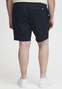 Mørkeblå shorts med en glat tekstur, der har to baglommer og en lige pasform, parret med hvide sneakers.