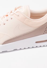 Nike sneakers feature a soft peach mesh upper, beige accents, white midsole, and textured sole with ventilation holes.