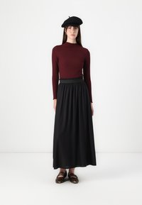 Burgundy ribbad långärmad topp, svart flödande maxikjol, svart basker och djurmönstrade skor kompletterar outfiten. En enkel och elegant design.