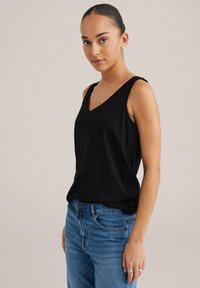 Top senza maniche nero con scollo a V, motivo a zigzag testurizzato e vestibilità rilassata. Abbinato a jeans in denim blu chiaro.