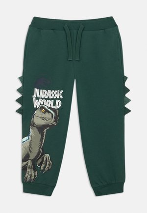 Grüne Sweatpants mit elastischem Bund, die ein Dinosaurier-Design und den Text "Jurassic World" zeigen. Seitliche Stacheln verleihen ein einzigartiges Designelement.