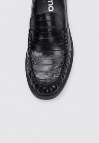 Mocasines de cuero sintético negro con upper texturizado, detalles de costura y punta redonda. Cuenta con una suela de goma para mayor comodidad y tracción.