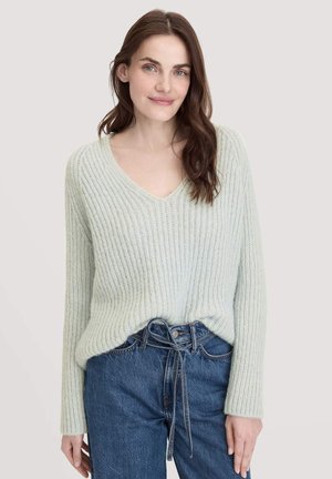  Lichtgroene V-hals trui in een textuurgebreide stof met ribgebreide details, gecombineerd met hoge blauwe jeans met een strikaccent op de taille.