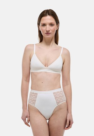 Femme portant un soutien-gorge triangle blanc et une culotte taille haute avec des panneaux latéraux transparents, debout devant un fond clair uni, face à l'avant.