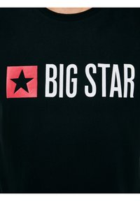 Czarna koszulka z białym napisem "BIG STAR" i czerwonym kwadratem z czarną gwiazdą na piersi.