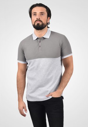 Camisa polo gris y gris claro con un diseño bicolor, de manga corta, cuello tipo polo y tapeta con tres botones. Textura de tela suave.