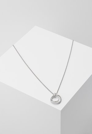 Collier chaîne en argent avec deux pendentifs circulaires entrelacés, l'un lisse et l'autre incrusté de petits cristaux, présenté sur une surface blanche.