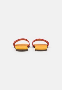 Röda och gula sandaler med platt sula och två böjda remmar, med en strukturerad fotbädd och en minimalistisk design.