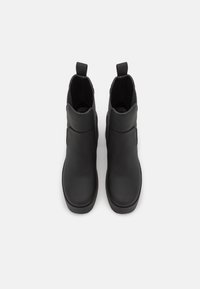 Botas de tobillo de cuero negro con un acabado liso, inserciones laterales elásticas y tiradores para facilitar su uso. Punta redondeada y suela de goma baja.