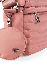 Bolso cruzado acolchado en color rosa con un monedero circular. Cuenta con herrajes plateados y una correa ajustable. Material de nylon suave con un ligero brillo.