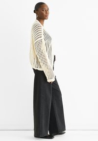 Knit cream sweater with open weave, paired with wide-leg black jeans. The top has long sleeves and a relaxed fit. Black flats complete the look.
