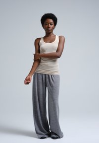 Beige aansluitend tanktop gecombineerd met loszittende grijze joggingbroek, voorzien van een trekkoord en zachte textuur, staande tegen een neutrale achtergrond.
