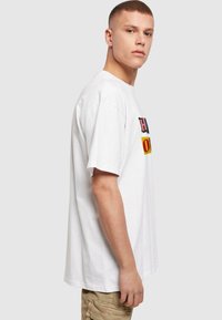 Hvid bomulds t-shirt med fed, farverig tekst på fronten. Løs pasform, korte ærmer og rund halsudskæring.