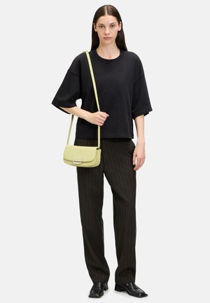 Maglietta nera oversize, pantaloni a righe con gamba larga e una borsa a tracolla in pelle verde con una forma strutturata e dettagli in metallo argentato.