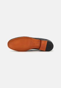 Semelle de chaussure en cuir tissé noir avec une incrustation en cuir orange lisse, présentant des coutures contrastées et un logo sur le talon.