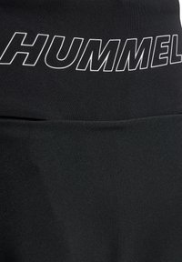 Svart sporttopp med vit "HUMMEL" text på övre delen, med en slät textur och figurnära design.