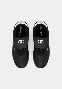 Pantofi sport negri cu un material texturat, accente albe și o talpă din cauciuc natural; prezintă un logo proeminent pe limbă și pe lateral.