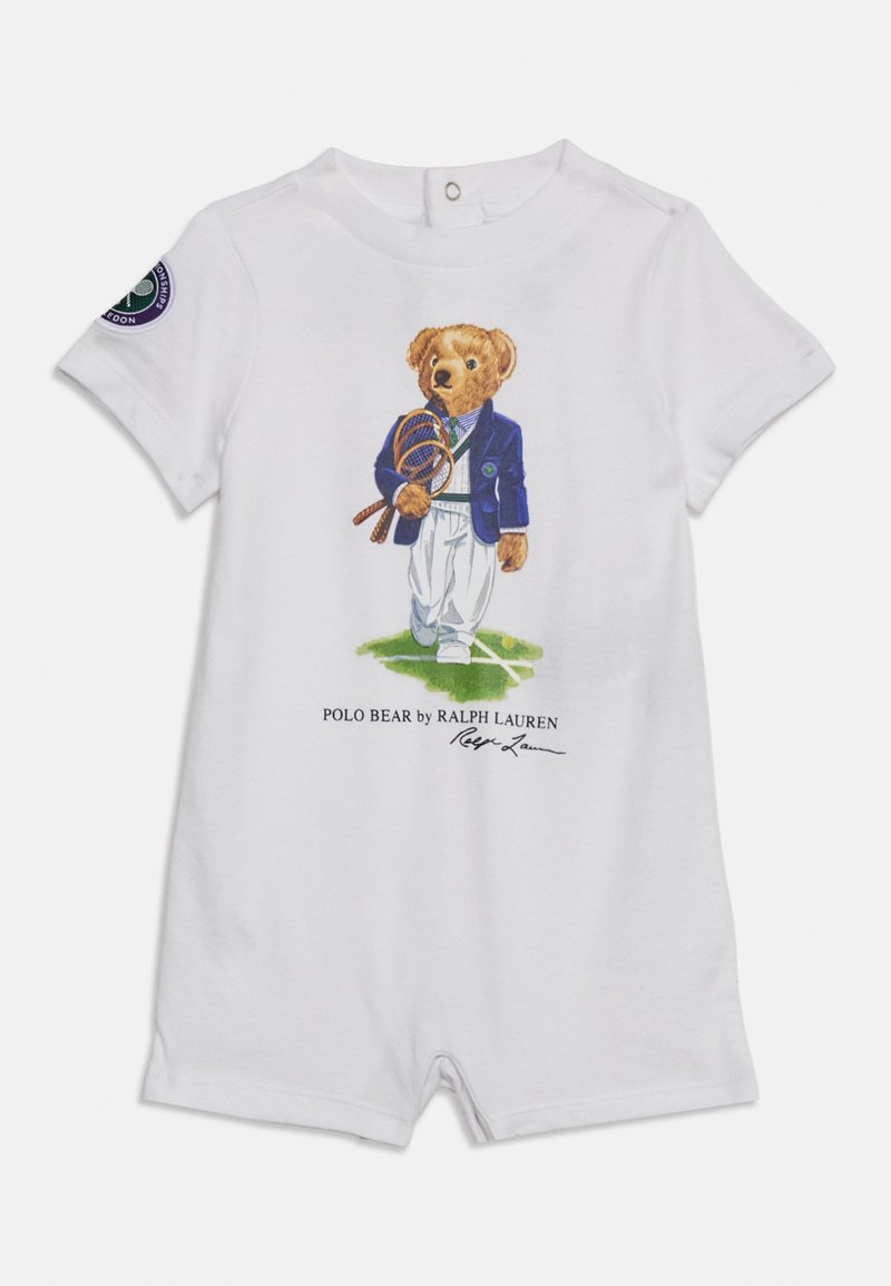 Barboteuse blanche pour bébé avec un ours jouant au tennis portant un blazer bleu marine et tenant deux raquettes de tennis sur le devant.
