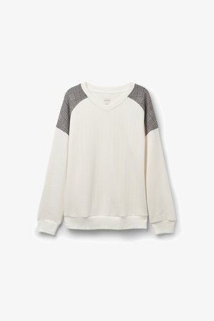 Vit ribbad sweatshirt med axeldetaljer i svart och vitt rutig mönster samt V-ringning. Har långa ärmar och en åtsittande nederkant.