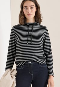 Zwart en grijs gestreepte hoodie van een gestructureerde stof, met een trekkoordkap en een relaxte pasvorm. Gecombineerd met donkerblauwe jeans.