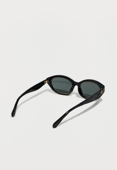 Lunettes de soleil ovales noires avec verres foncés et accents dorés, vues en angle arrière sur un fond blanc.
