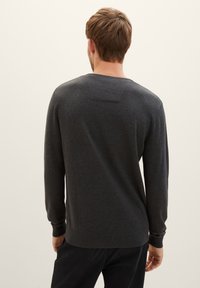 Suéter gris oscuro de manga larga, con cuello redondo y puños acanalados. Textura lisa con un sutil patrón de punto. Vista desde atrás.