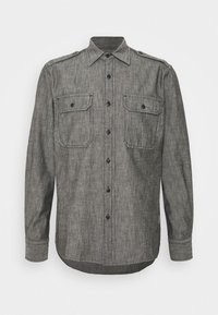 Camicia grigia a maniche lunghe con bottoni, dotata di due tasche frontali con patta e spalline, esposta su uno sfondo bianco.