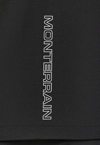 Texte vertical blanc contouré 'MONTERRAIN' sur fond en tissu noir, centré et en gras.