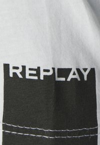 Sort-hvide stribede stof med logoet "REPLAY" i fede hvide bogstaver, med synlig sømdetalje.