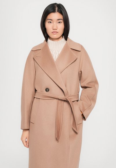 Beige wool blend coat with a belted waist, large lapels, double button closure, and side pockets. Textured knit sweater underneath.
