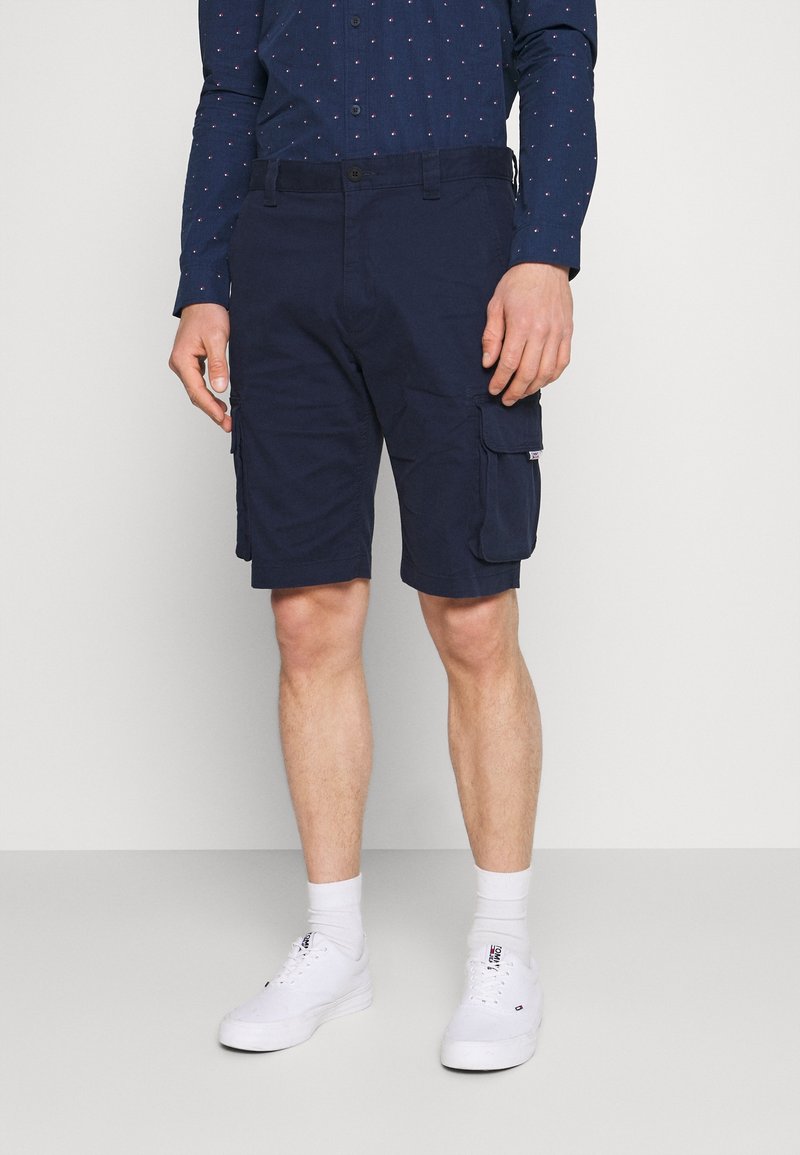 Pantalones cortos cargo azul marino con múltiples bolsillos, fabricados con tela duradera, presentan un ajuste relajado y se combinan con zapatillas blancas y calcetines.