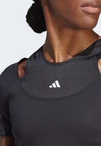 Svart träningslinné med rund halsringning, texturerat tyg, urklippta axlar och en vit Adidas-logotyp på bröstet.