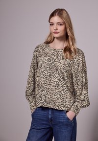 Blouse légère à manches longues imprimé léopard en beige et noir, avec un col rond et une coupe décontractée, associée à un jeans bleu.