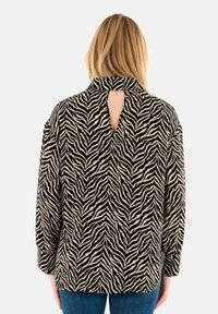 Top a strisce zebrate nero e crema con maniche lunghe, colletto e un'apertura a chiave sulla schiena. Tessuto testurizzato con vestibilità comoda.