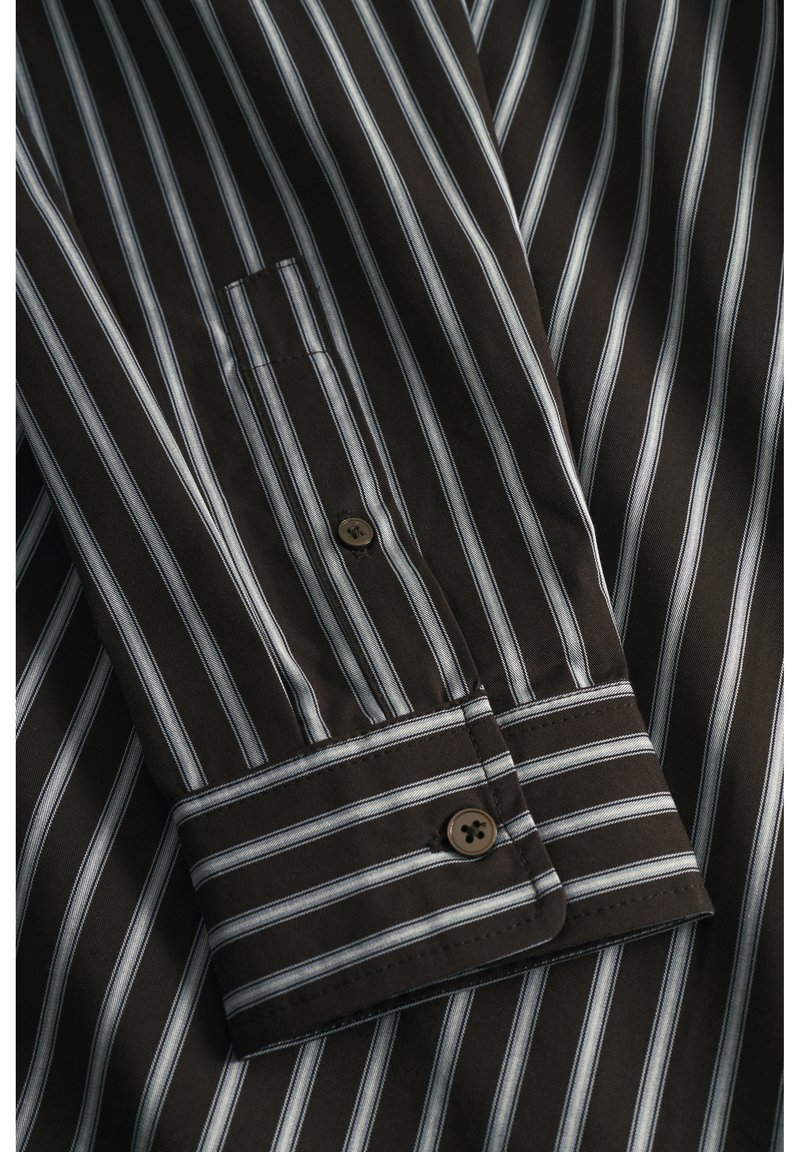 Chemise rayée brune avec des rayures blanches et bleu clair verticales, fermeture à boutons, et un poignet structuré avec un détail de bouton foncé.
