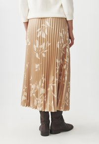 Jupe maxi plissée beige avec un motif floral en blanc cassé. Fabriquée en tissu léger, elle présente une taille haute et un design fluide.