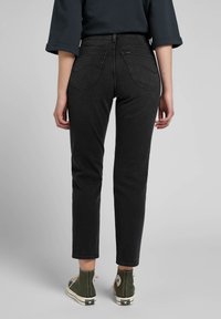 Black denim pants with a slim fit, featuring back pockets, straight legs, and a mid-rise waist. Worn with olive green high-top sneakers.