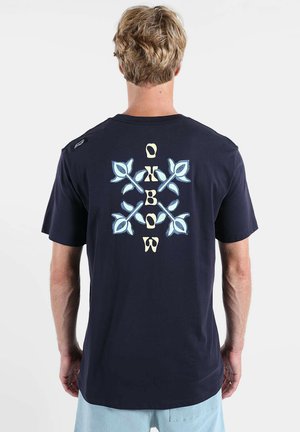 T-shirt bleu marine à manches courtes, arborant un motif floral central en impression bleu clair et jaune au dos, avec un marquage sur l'épaule.