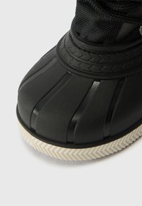 Fekete gumicsizma textúrázott, bordázott dizájnnal. Jellemzője egy fehér chevron mintás talp és egy sima orr rész.