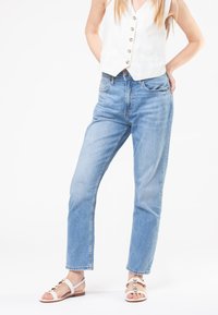Light blue denim jeans with a straight-leg cut, featuring a zip fly, five-pocket design, and subtle fading. Paired with white sandals.