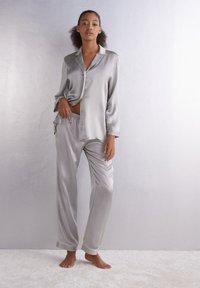 Grijs satijnen pyjama set met lange mouwen, knoopsluiting aan de bovenkant en broek met elastische tailleband. Gladde textuur en contrasterende afwerking op de manchetten.