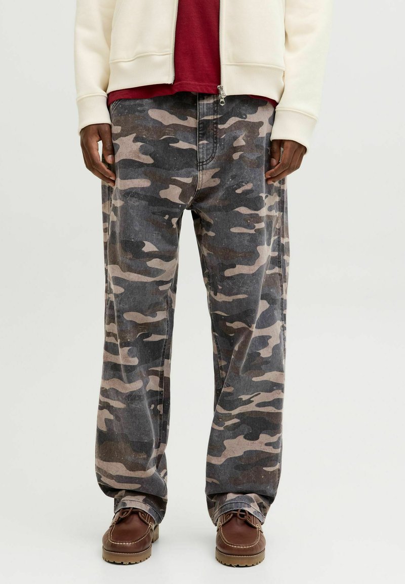 Pantalon en camouflaged gris avec des motifs beiges, coupe décontractée, et zip à l'avant. Assorti à des mocassins marron.