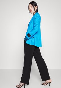 Um blazer ajustado azul claro, calças pretas de cintura alta e sapatos de salto preto com tiras. O blazer tem um colarinho com lapelas e punhos contrastantes.