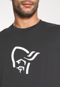 Svart bomulls t-skjorte med et stort, grafisk hvitt logo av et hjelmdesign sentrert på brystet, med klassisk rund hals.
