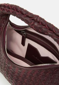 Sac en cuir bordeaux avec un extérieur tissé, doté d'une fermeture zippée et d'une doublure en tissu rose. Comprend une poche intérieure avec une étiquette en cuir.