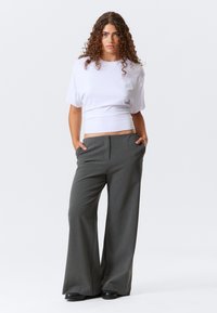 Haut blanc à manches courtes avec une taille ajustée, associé à un pantalon large à rayures gris, doté de poches latérales et d'une texture lisse.