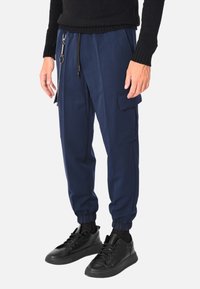 Pantaloni jogger blu navy in materiale morbido con vita elastica, tasche laterali e dettaglio a catena. Abbinati a sneakers nere.